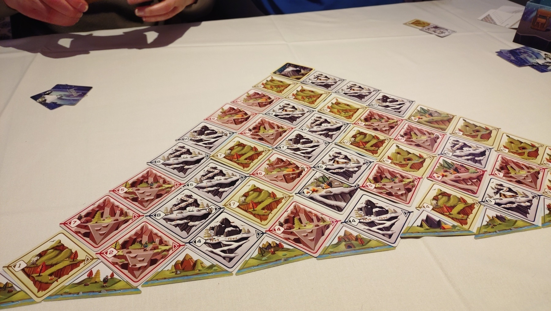 A finished game of "Tranquility: The Ascent", a triangle of cards laid out on the table, square cards corner side down, at the top is the summit card