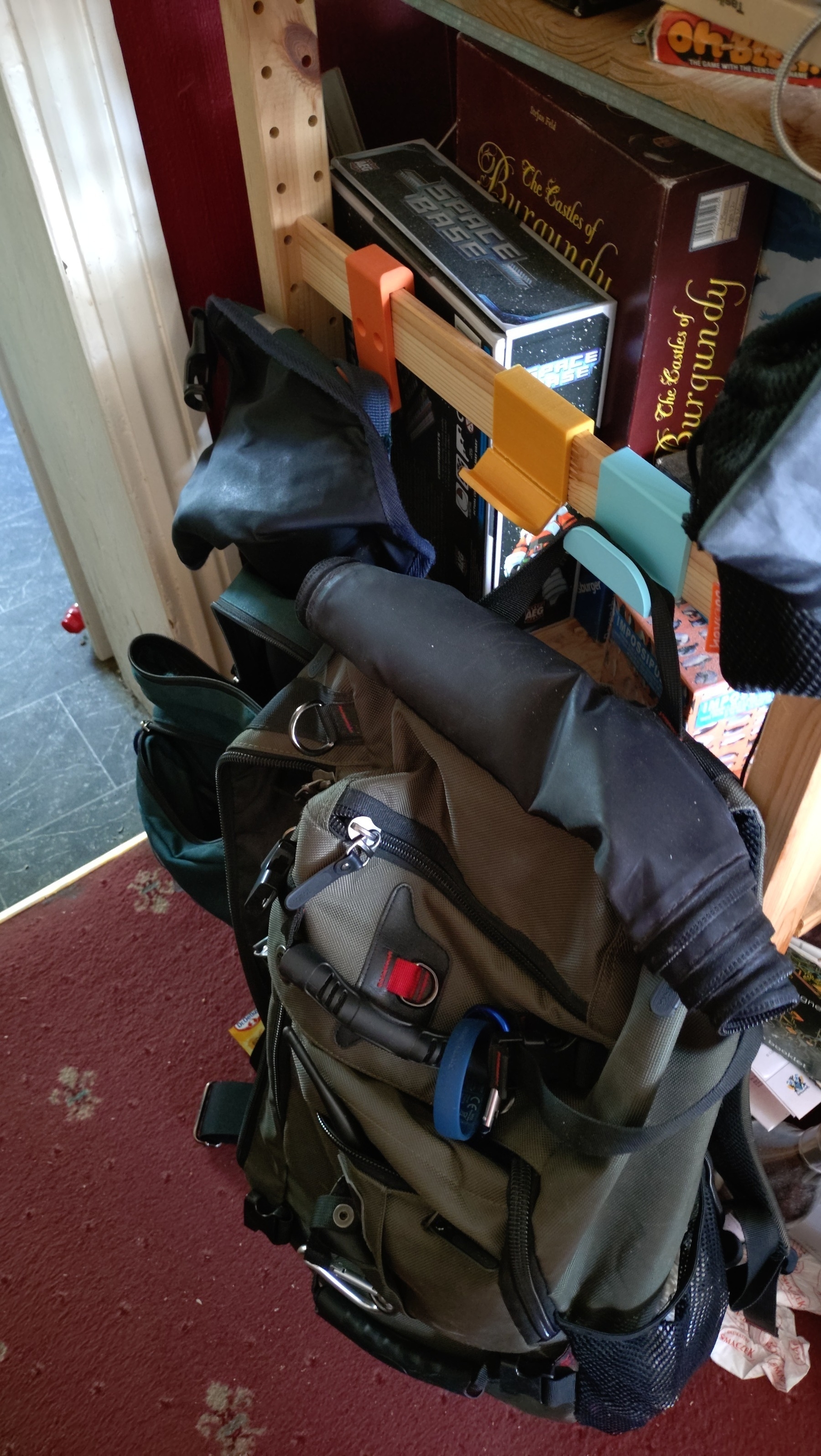 The side of an Ikea Ivar shelving with two backpacks hanging from 3d printed hooks. In between the bags is a third printed hook which has broken