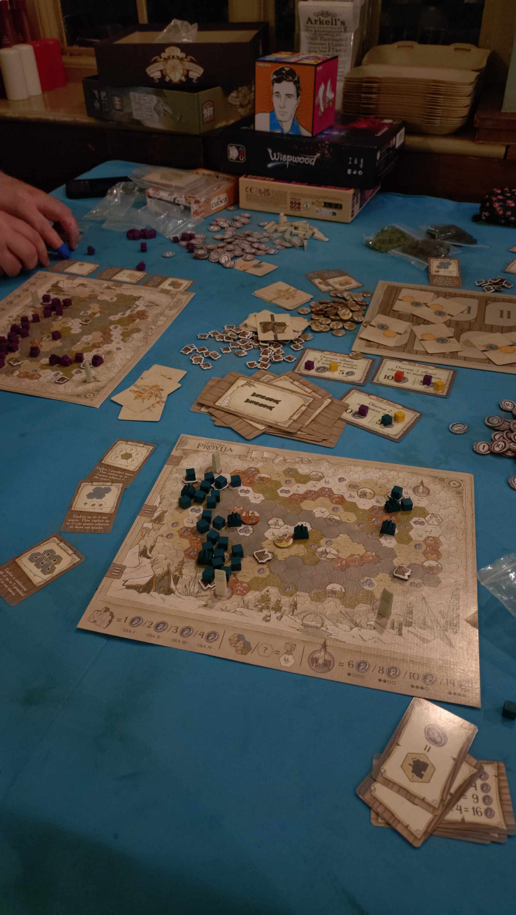 Guild of Merchant Explorers endgame, centre of the table are the round cards. In the foreground is my game sheet showing several dark blue cubes and three towers on a map&10;